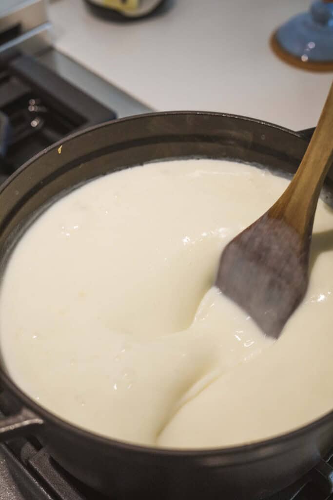 Wooden spoon stirs pot full of creamy broth base.