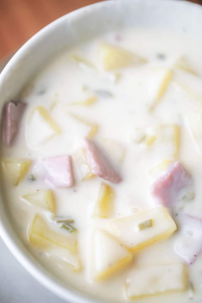 Chunks of potato and cubes of ham are served in a creamy and hearty broth in a white bowl.