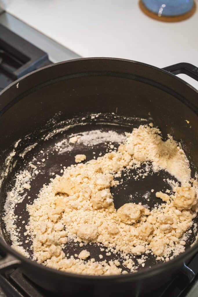 Flour is mixed with melted butter in a large black pot for making a rue.