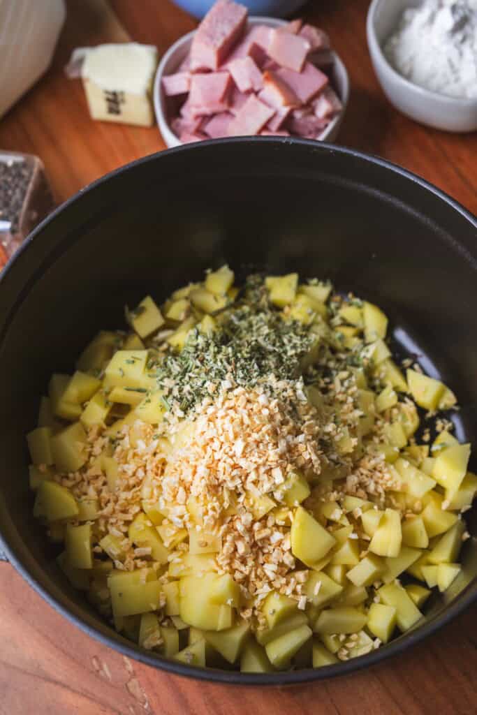 Raw cubed potatoes, dried celery and onions sit in the bottom of a large black pot.