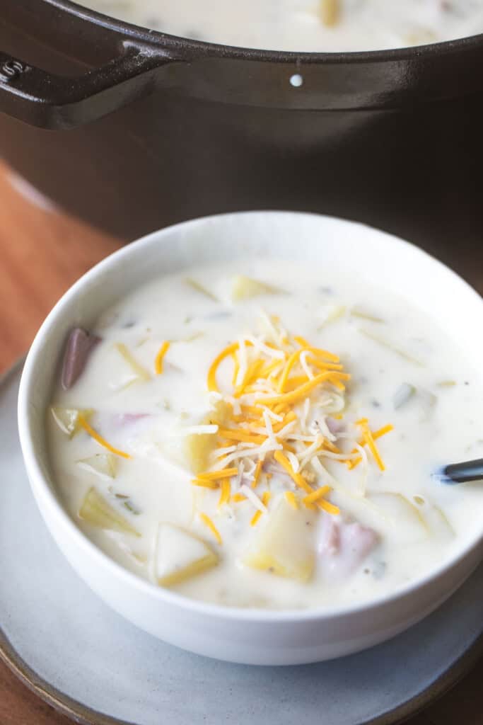 Bowl of potato soup is served in bowl and topped with shredded cheese.