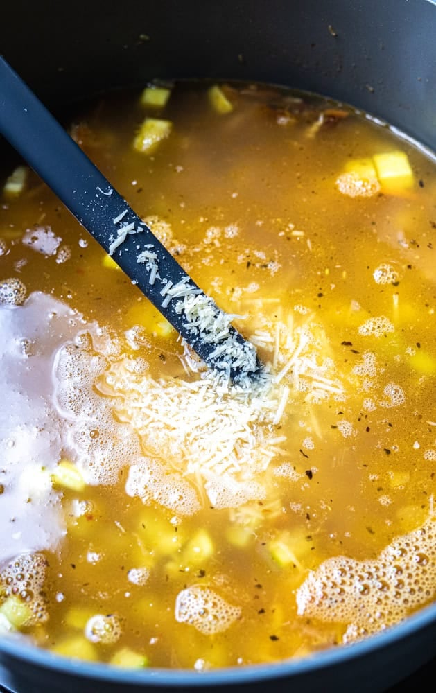 Broth and parmesan added to large pot where soup cooks.