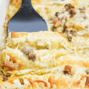 Golden brown Breakfast Enchiladas sit in a baking dish ready to serve with a spatula.