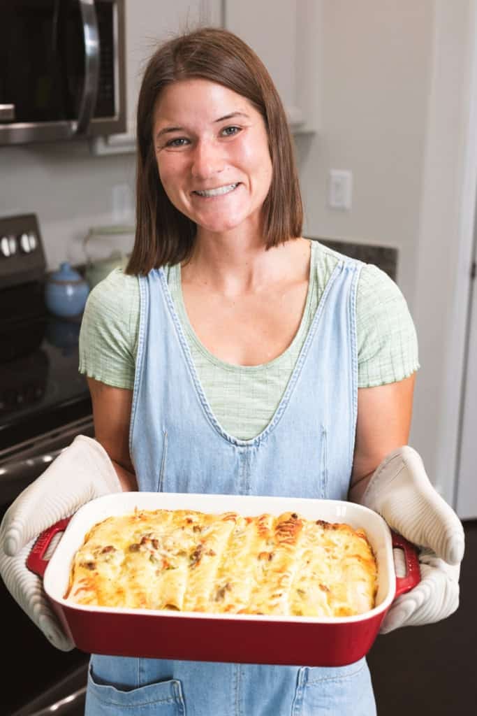 Ashley holds a pan of warm golden brown enchiladas pulled from the oven.