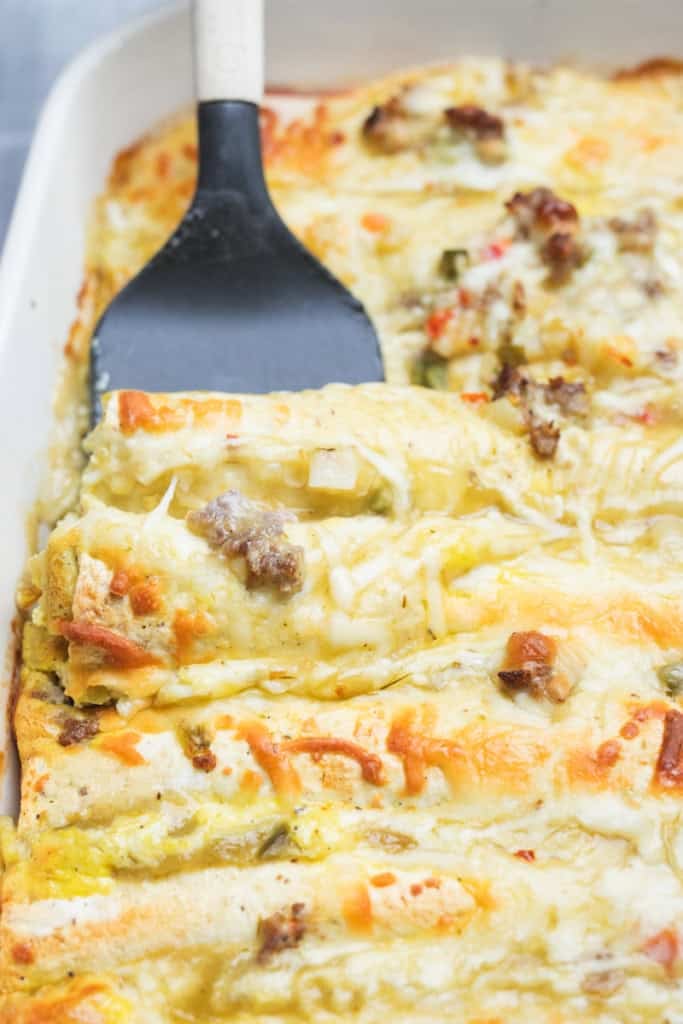A spatula scoops up a serving of golden brown and cheesy Breakfast Enchiladas.