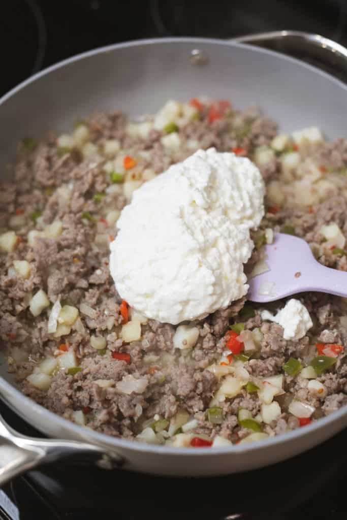 Cottage cheese is added to a skillet of browned sausage, hash browns, peppers and onions.