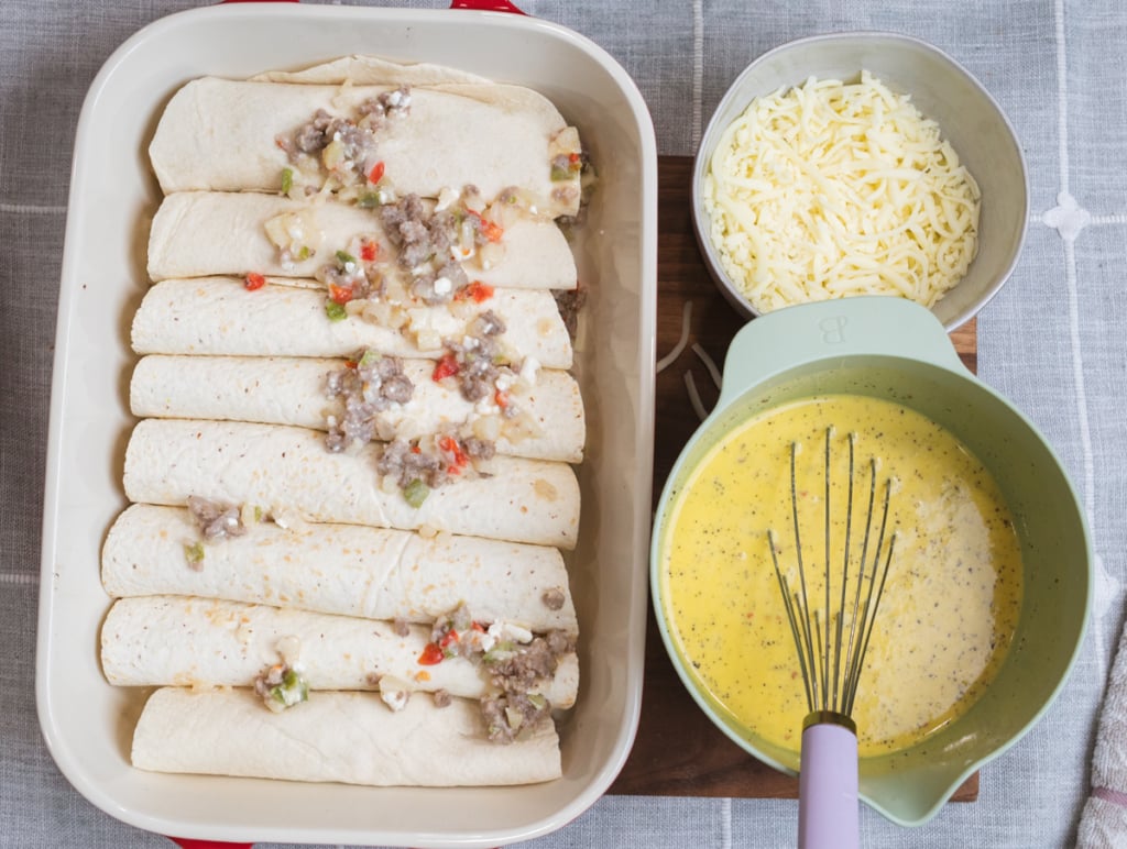 Filled tortillas sit in a baking dish beside a bowl of egg mixture ready to be poured over the top.