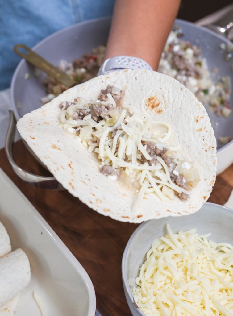 Shredded cheese is added to a tortilla with sausage, potatoes, onions and peppers.