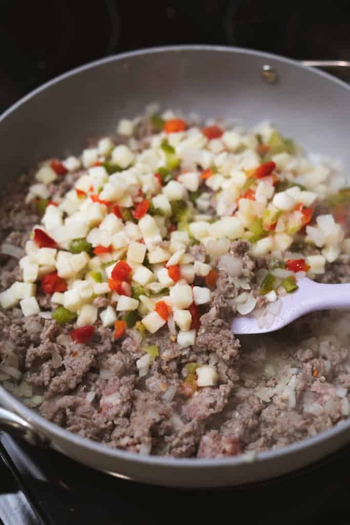 Diced potatoes, peppers, onions, ground sausage sit in a large skillet to brown.