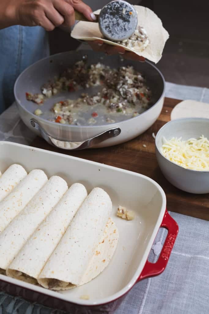 A measuring cup scoops a sausage and potato mixture on a tortilla.