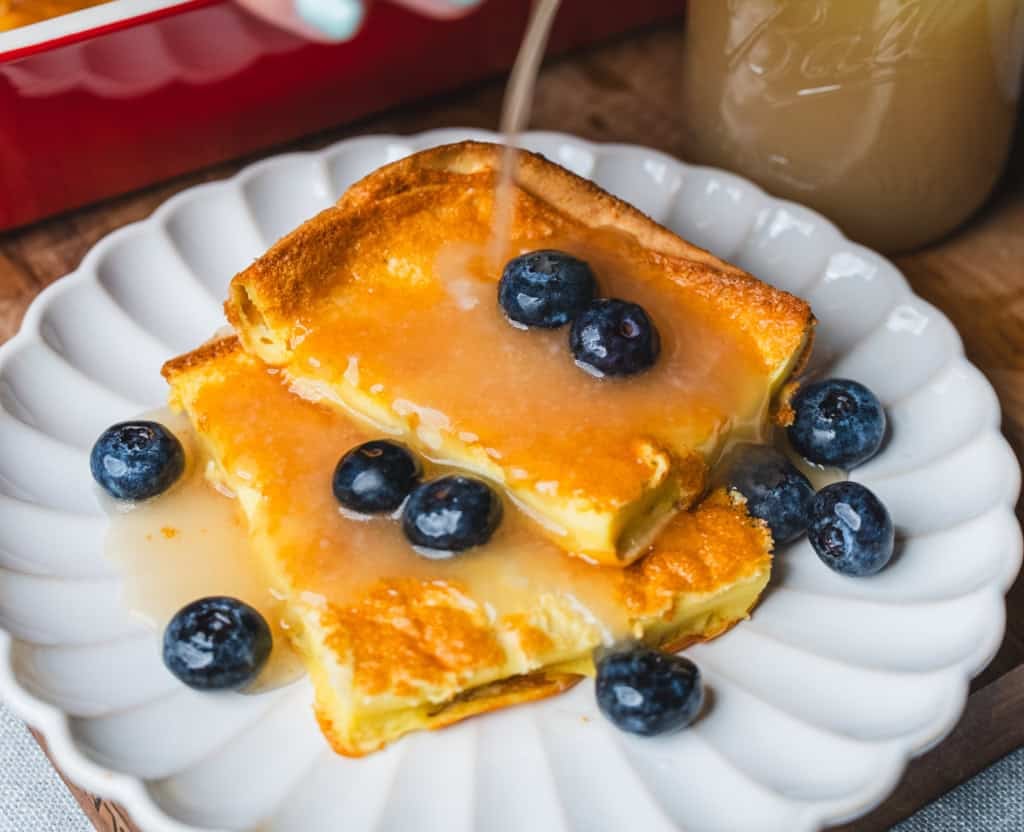 Warm coconut syrup is poured over the top of German pancakes that sit on a plate topped with fresh blueberries.
